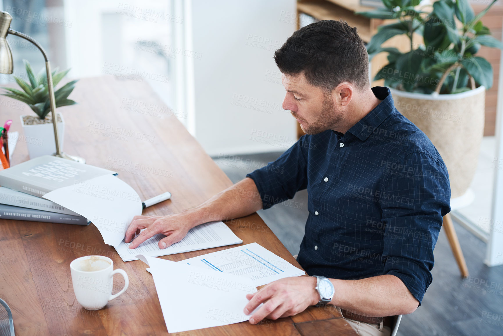 Buy stock photo Shot of a handsome mature businessman looking through some paperwork while sitting in his office