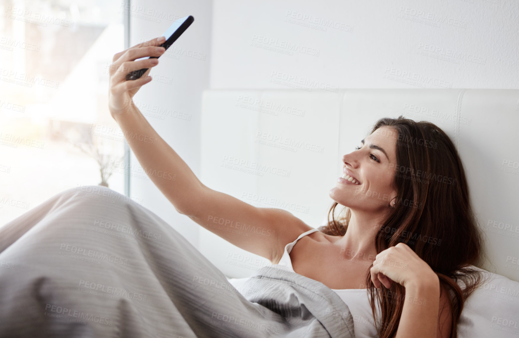 Buy stock photo Shot of a beautiful young woman talking selfies while lying in bed