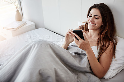 Buy stock photo Shot of a young woman using her cellphone while lying in bed