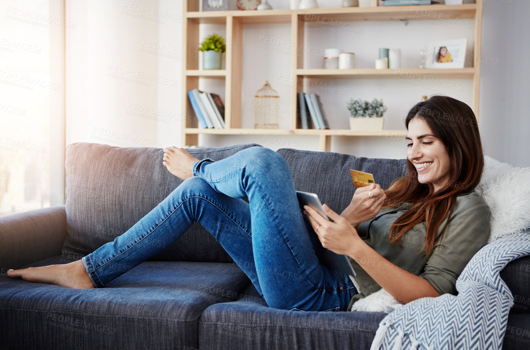 Buy stock photo Shot of a young doing online shopping while relaxing on her couch at home