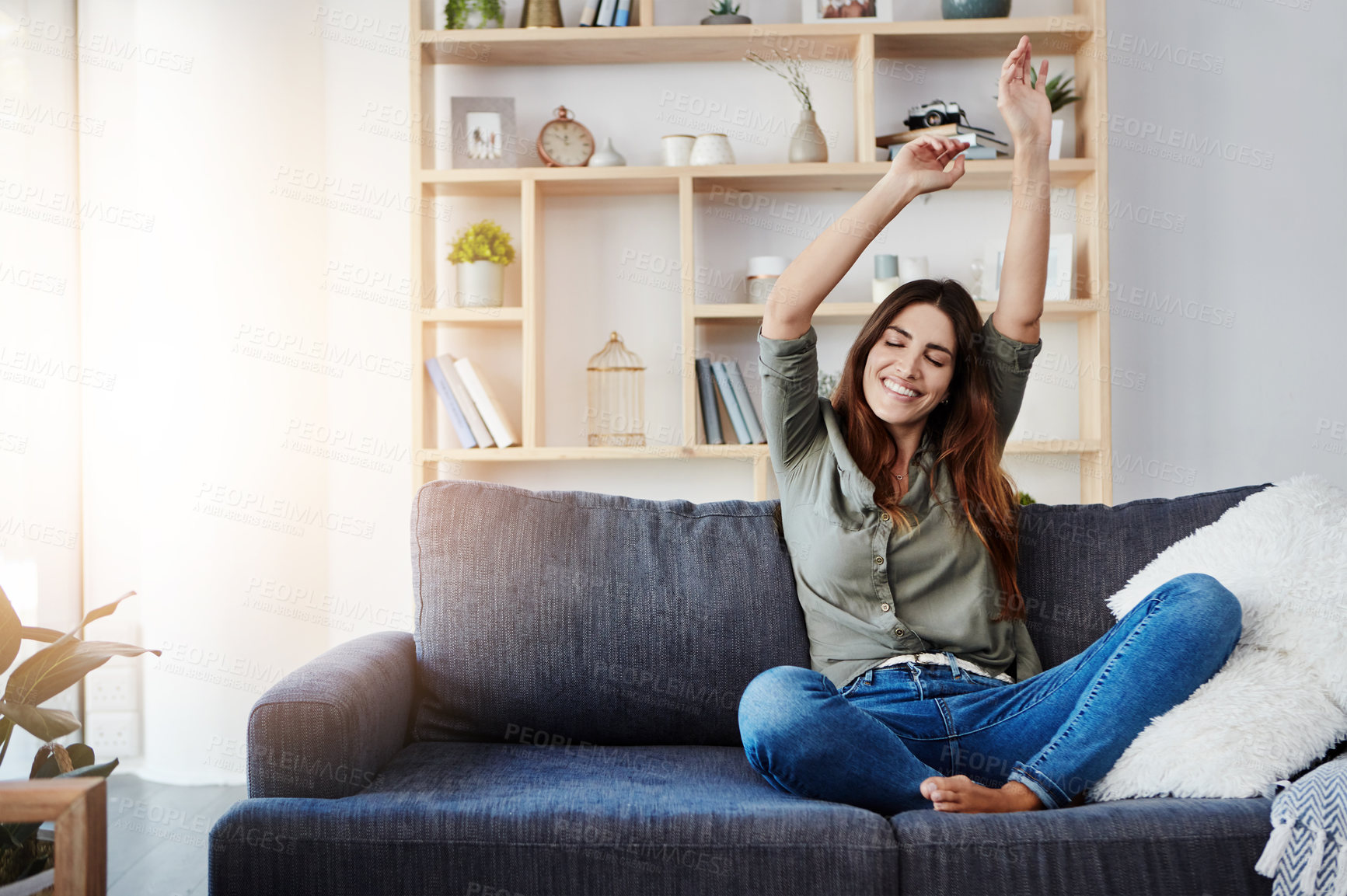 Buy stock photo Shot of a happy young woman dancing while sitting on her sofa at home
