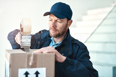 Buy stock photo Shot of a handsome delivery man sealing a package while out making deliveries