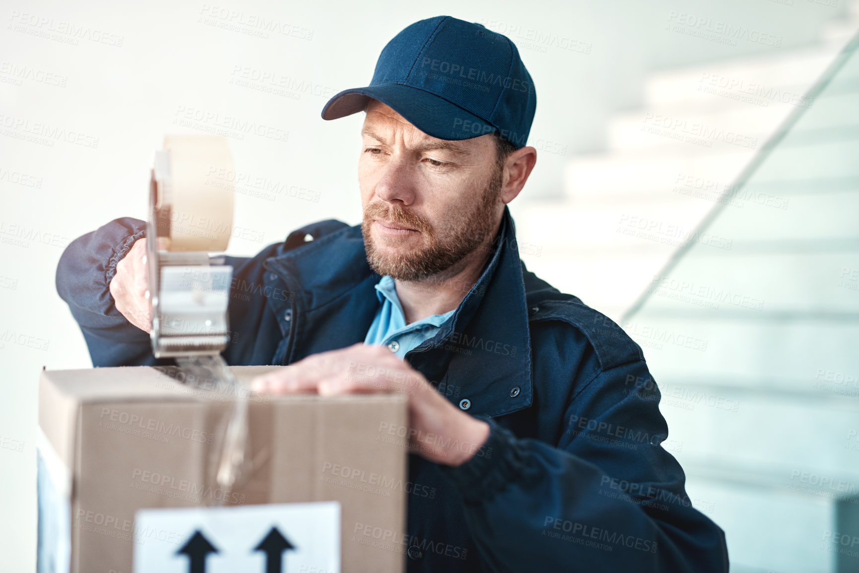 Buy stock photo Shot of a handsome delivery man sealing a package while out making deliveries