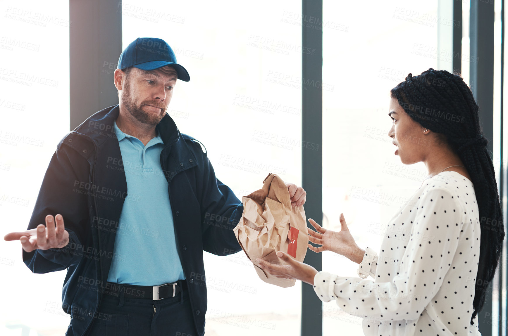 Buy stock photo Shot of a handsome delivery man negotiating with a dissatisfied female customer in the lobby