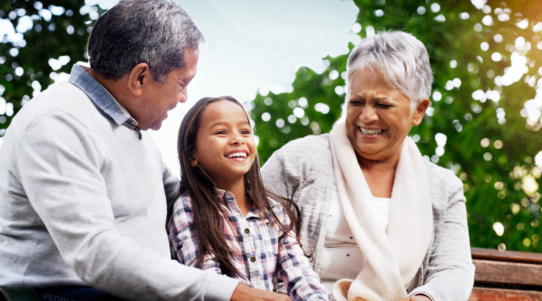 Buy stock photo Park, bench and grandparents with child, laughing and bonding on outdoor adventure together. Old man, senior woman and girl in backyard with love, happiness and family fun in nature with grandchild