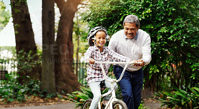 Buy stock photo Shot of an adorable little girl being taught how to ride a bicycle by her grandfather at the park