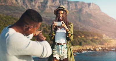 Buy stock photo Couple, photography and beach with phone for road trip, memory or outdoor moment together in nature. Woman or photographer taking picture of man, boyfriend or partner with mobile smartphone by ocean