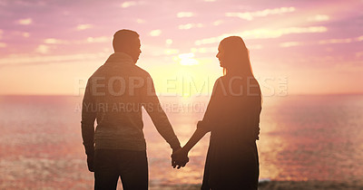 Buy stock photo Rearview shot of a happy young couple holding hands at sunset on the beach
