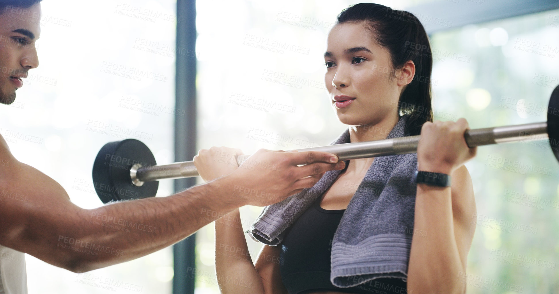 Buy stock photo Cropped shot of an attractive young sportswoman lifting a barbell with the help of her fitness coach in a gym