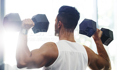 Buy stock photo Rearview shot of a handsome young sportsman working out with dumbbells in a gym