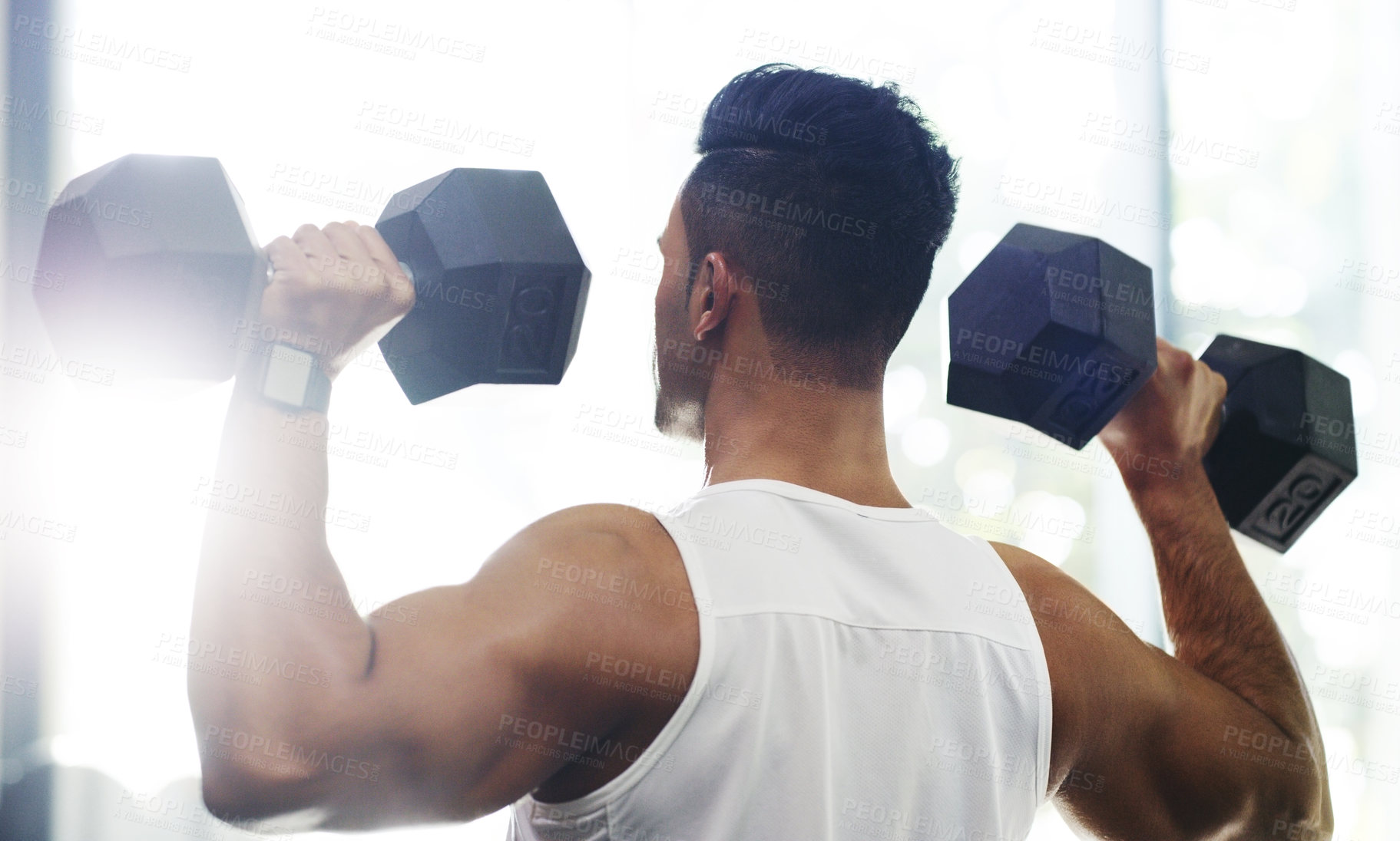 Buy stock photo Rearview shot of a handsome young sportsman working out with dumbbells in a gym