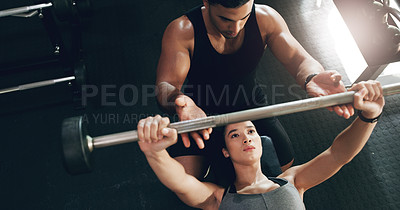 Buy stock photo Shot of a focused young woman lifting weights with her personal trainer assisting her