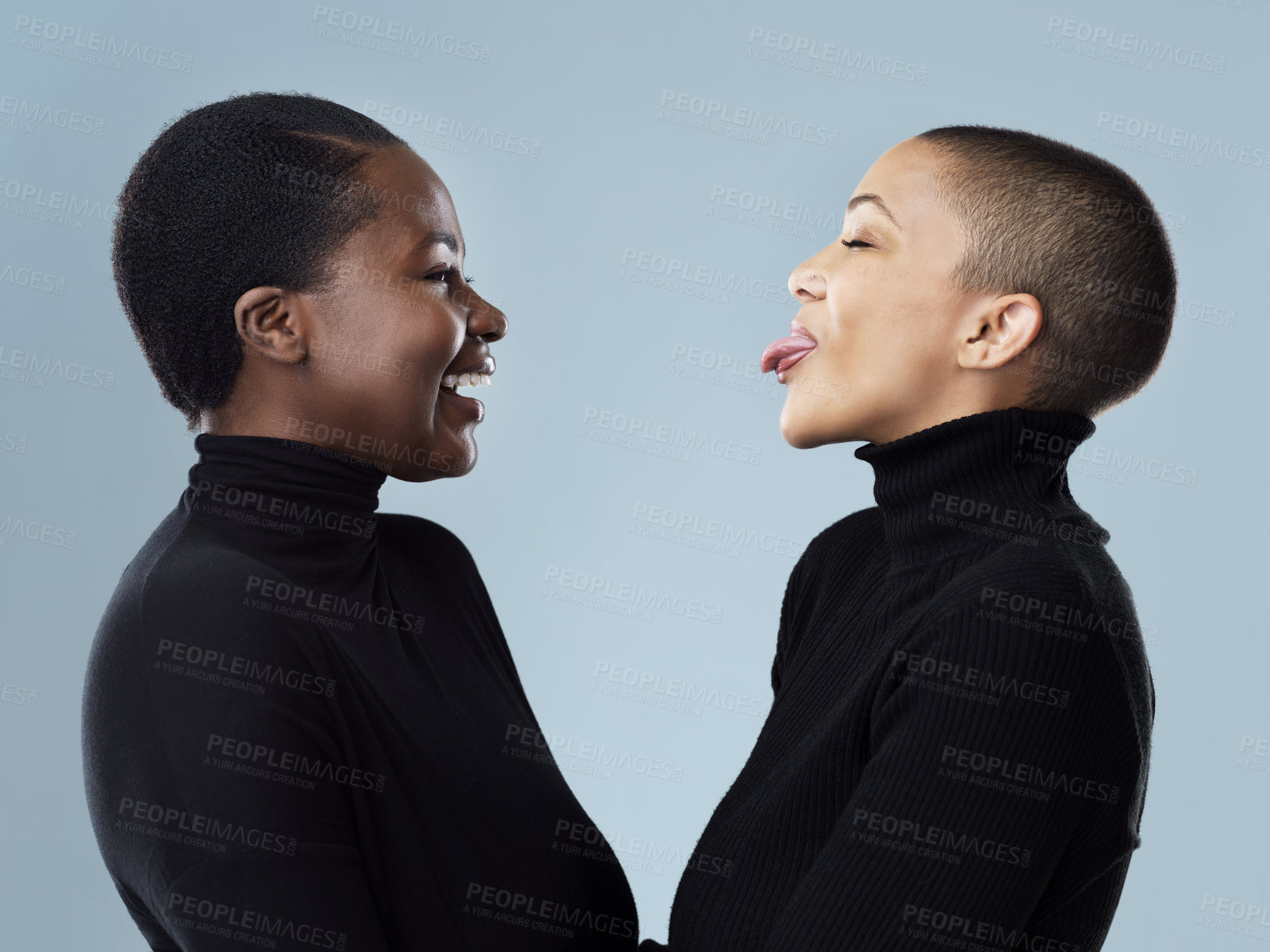 Buy stock photo Studio shot of two beautiful young women pulling faces to each other while standing against a grey background