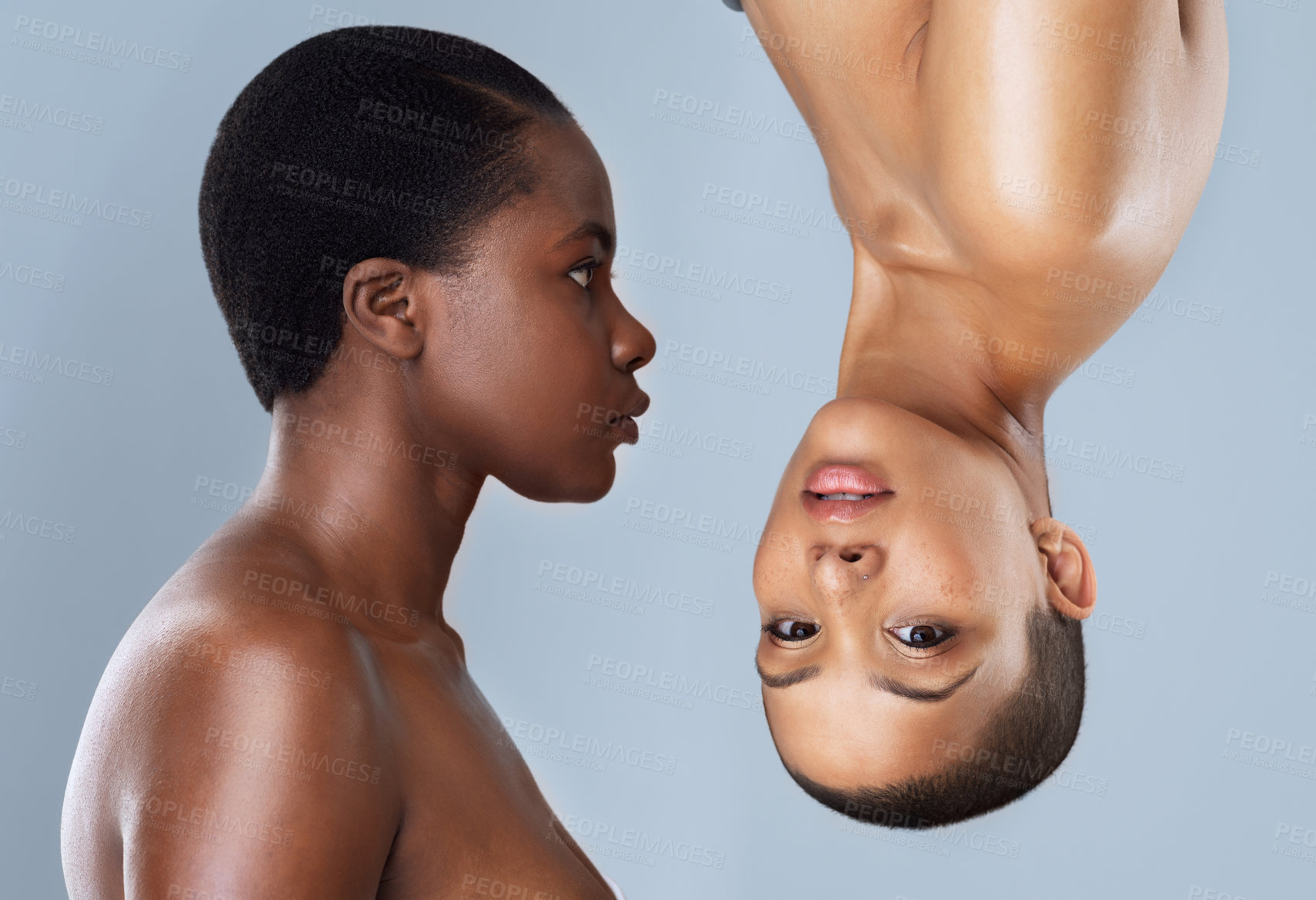 Buy stock photo Portrait of two beautiful young women standing close  to each other with one upside down against a grey background