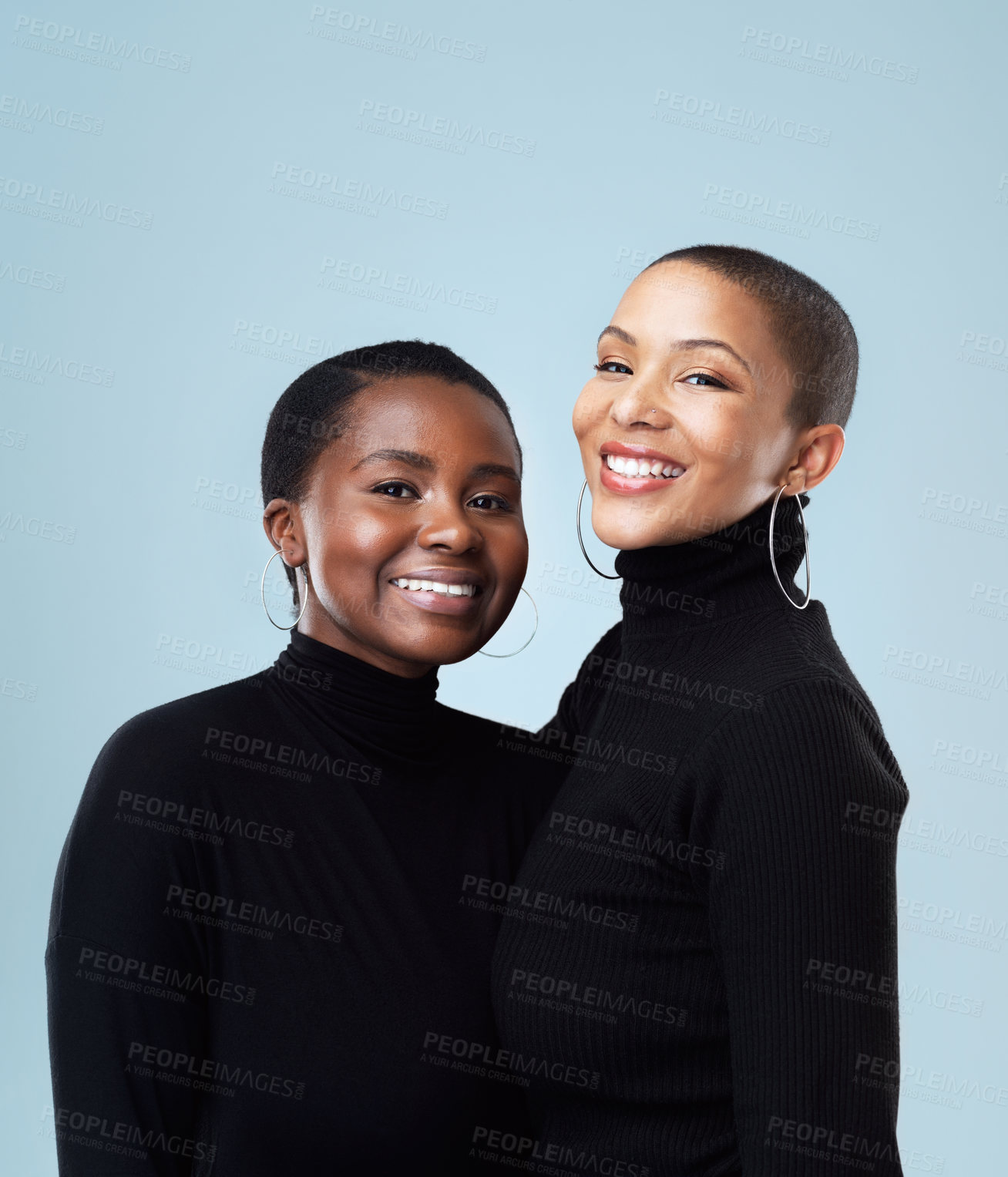 Buy stock photo Portrait of two beautiful young women holding each other while standing against a grey background