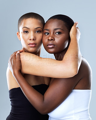 Buy stock photo Portrait shot of two beautiful young women holding each other while standing against a grey background