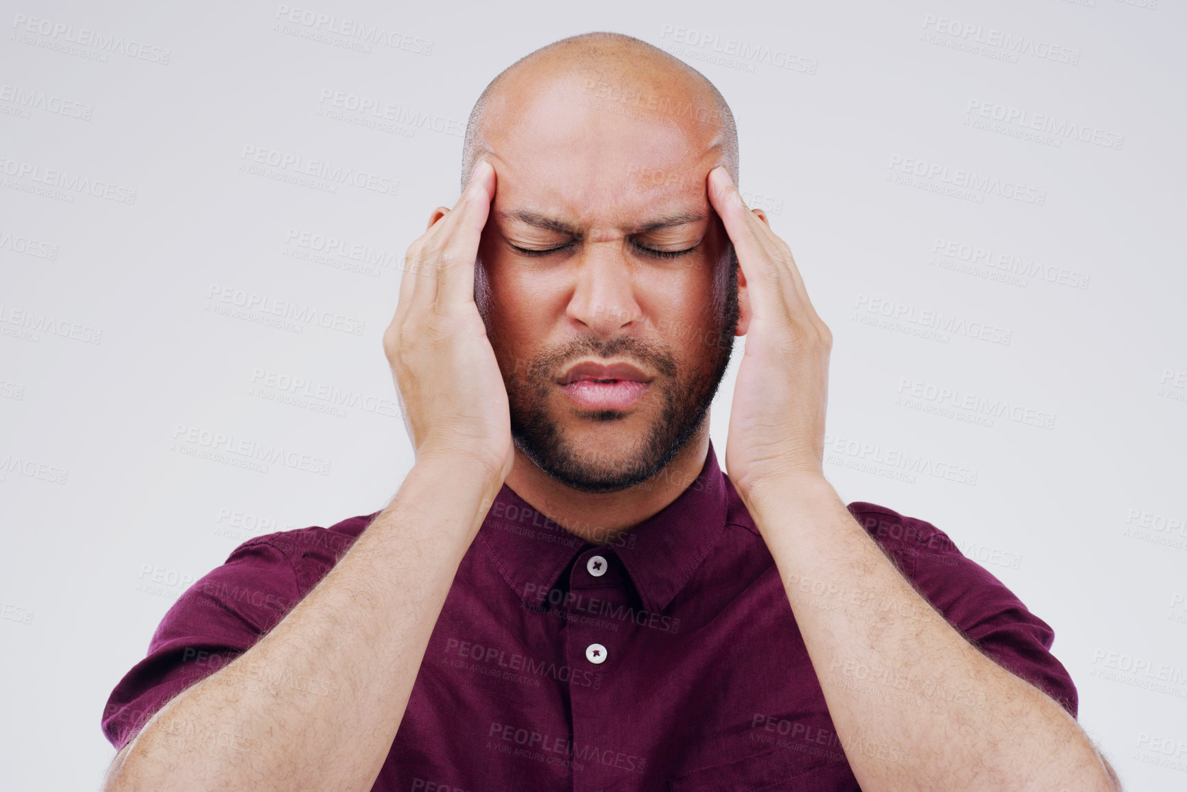Buy stock photo Shot of a young man holding his head while suffering from a headache against a grey background
