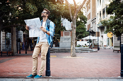 Buy stock photo Full length shot of a handsome young man looking at a map while touring a foreign city