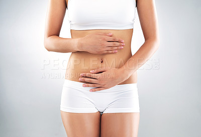 Buy stock photo Studio shot of an unrecognizable woman holding her stomach against a grey background