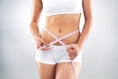 Buy stock photo Studio shot of an unrecognizable fit young woman measuring her waist against a grey background