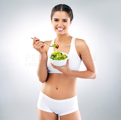 Buy stock photo Studio portrait of an attractive young woman eating a bowl of salad against a grey background