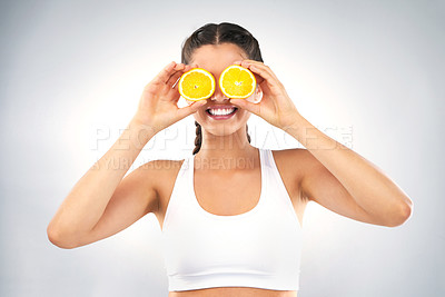 Buy stock photo Studio shot of a healthy young woman holding up oranges in front of her eyes against a grey background