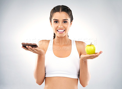 Buy stock photo Studio portrait of a beautiful young woman deciding between healthy and unhealthy foods against a grey background