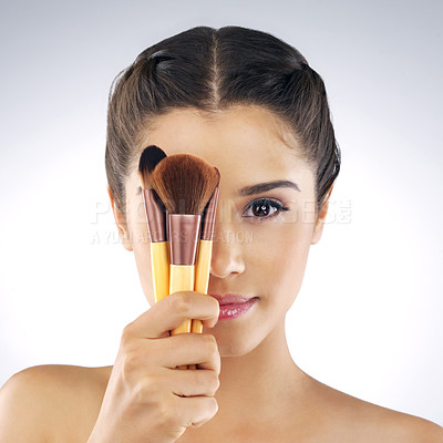 Buy stock photo Studio portrait of a beautiful young woman holding up makeup brushes against her face against a grey background