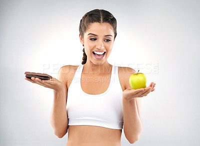 Buy stock photo Studio portrait of a beautiful young woman deciding between healthy and unhealthy foods against a grey background