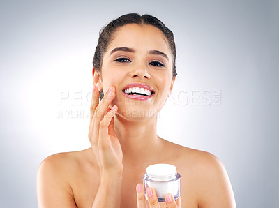 Buy stock photo Portrait of a beautiful young woman holding a tub of moisturizer and applying it to her face in studio