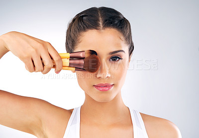 Buy stock photo Studio portrait of a beautiful young woman holding up makeup brushes against her face against a grey background