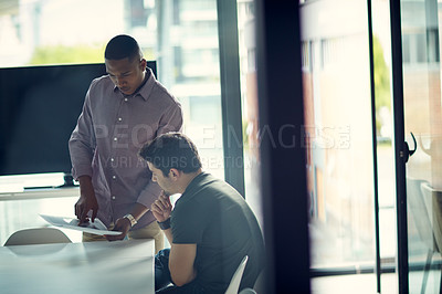 Buy stock photo Shot of two young businessmen going over paperwork together in a modern office