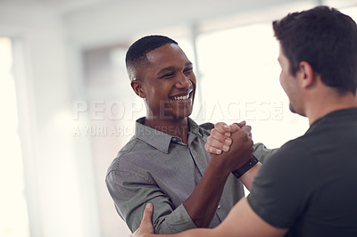 Buy stock photo Shot of two young businessmen gripping hands in solidarity in a modern office