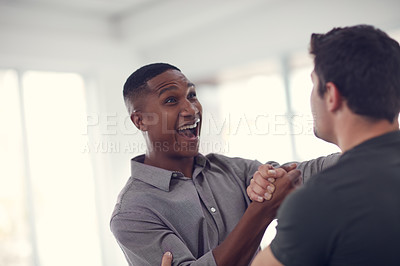 Buy stock photo Shot of two young businessmen gripping hands in solidarity in a modern office