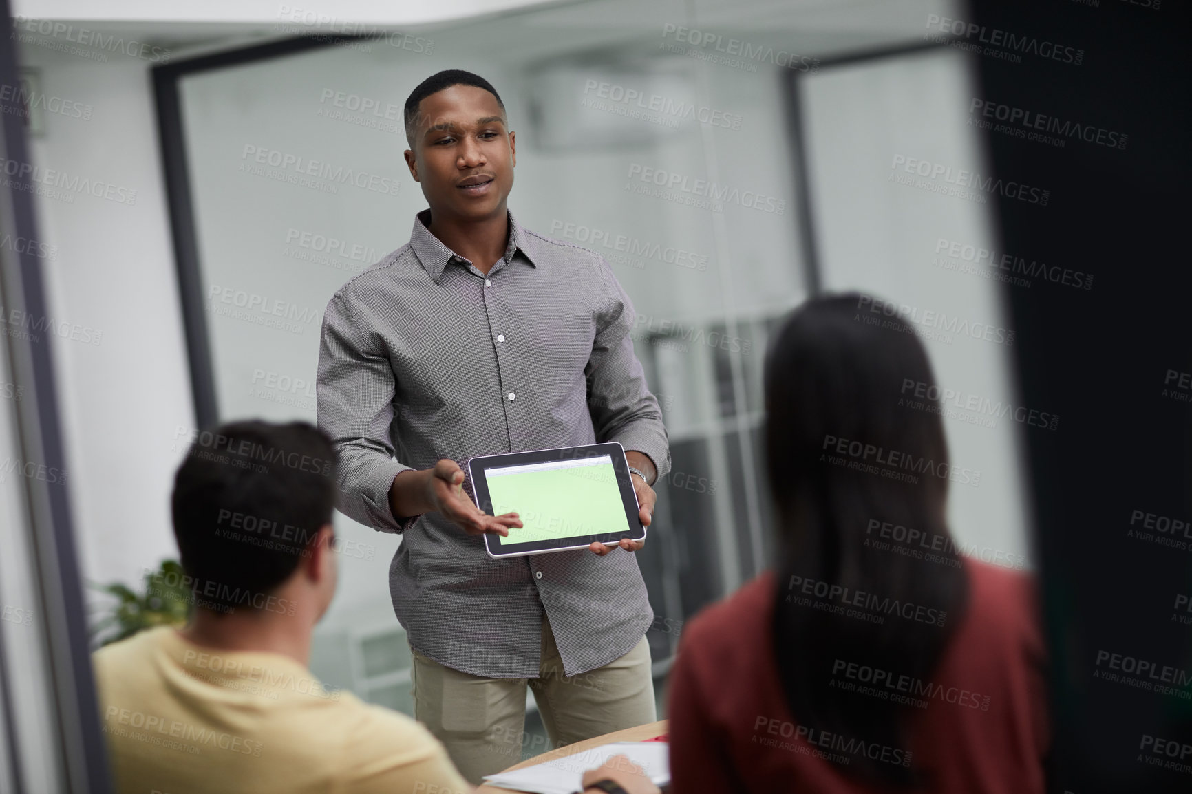 Buy stock photo Shot of a young businessman using a digital tablet during a meeting with colleagues in a modern office