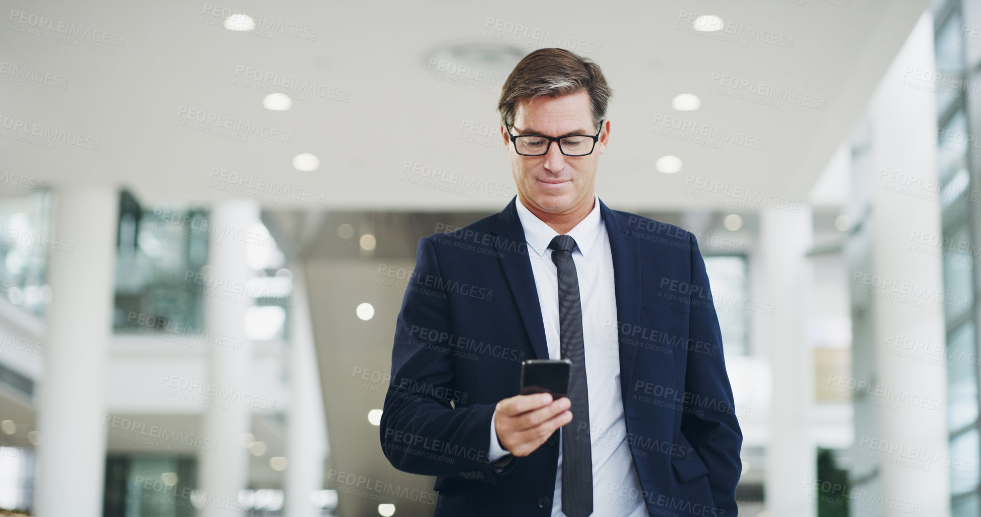 Buy stock photo Cropped shot of a mature businessman using a smartphone while walking through a modern office
