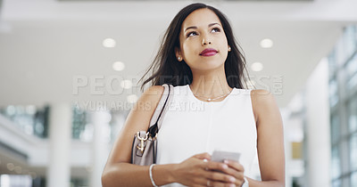 Buy stock photo Cropped shot of a young businesswoman using a smartphone while walking through a modern office