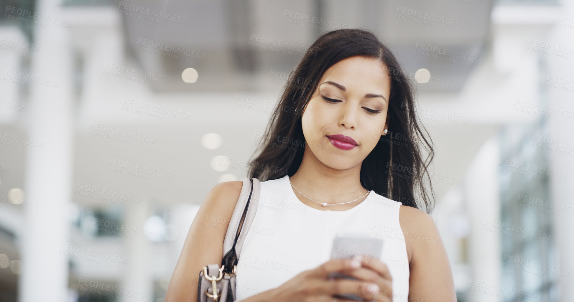 Buy stock photo Cropped shot of a young businesswoman using a smartphone while walking through a modern office