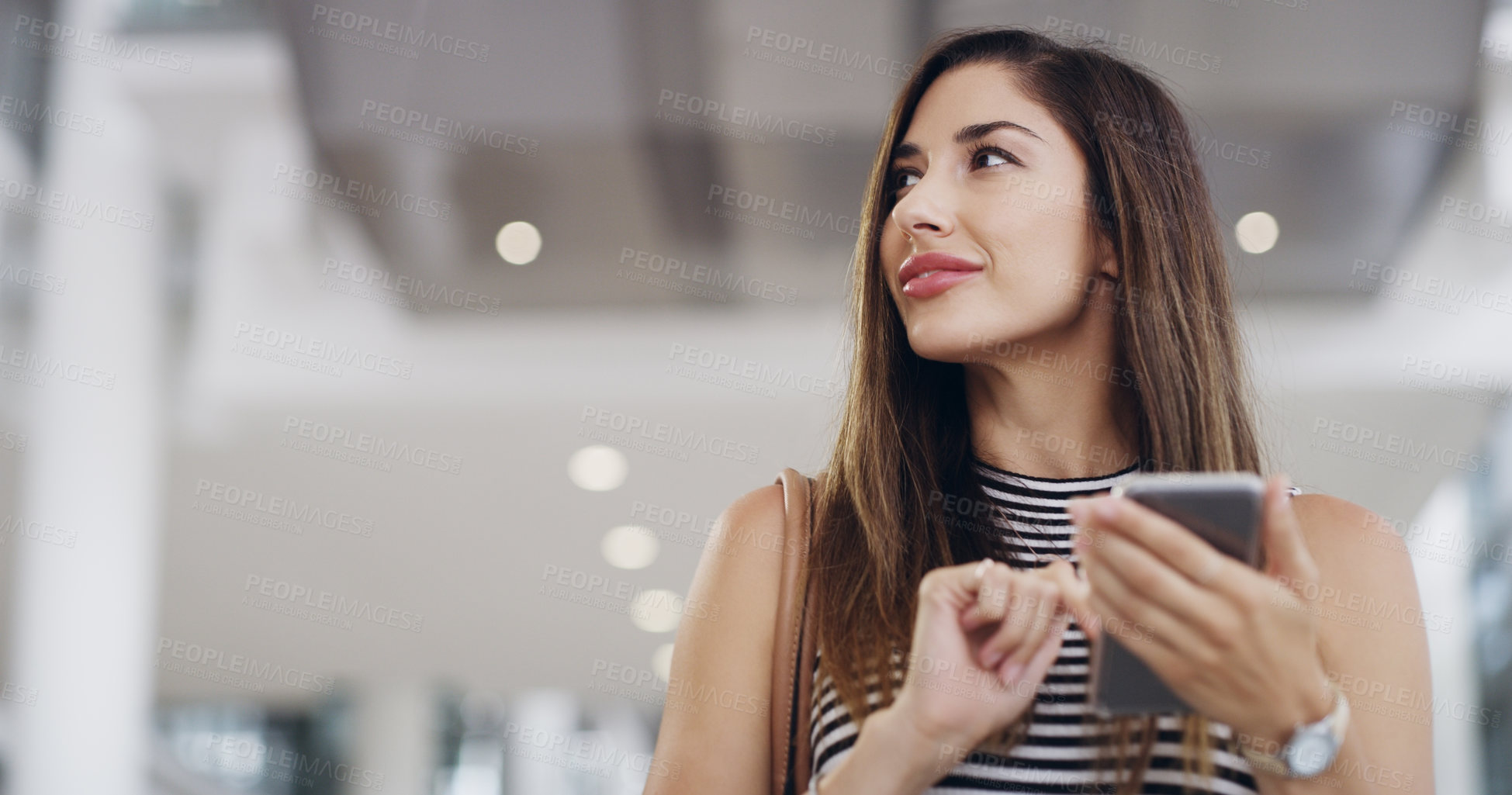 Buy stock photo Cropped shot of a young businesswoman using a smartphone while walking through a modern office