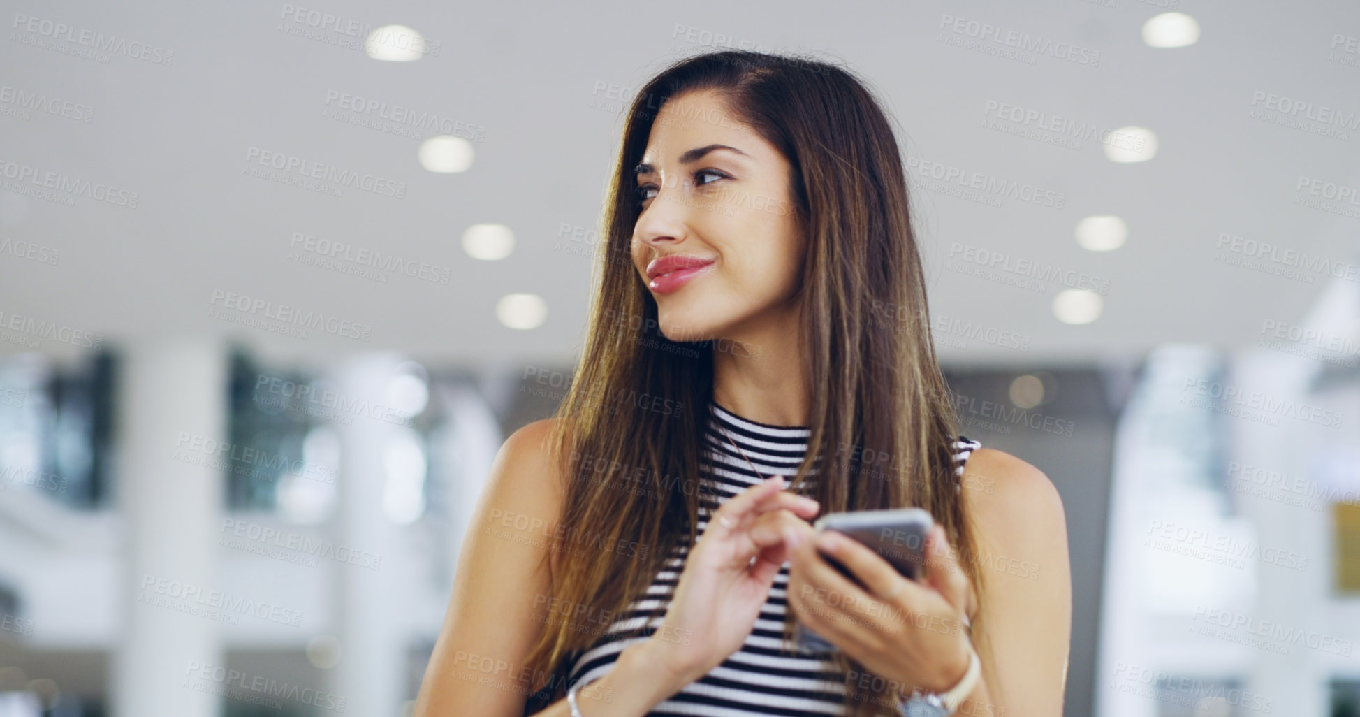 Buy stock photo Cropped shot of a young businesswoman using a smartphone while walking through a modern office