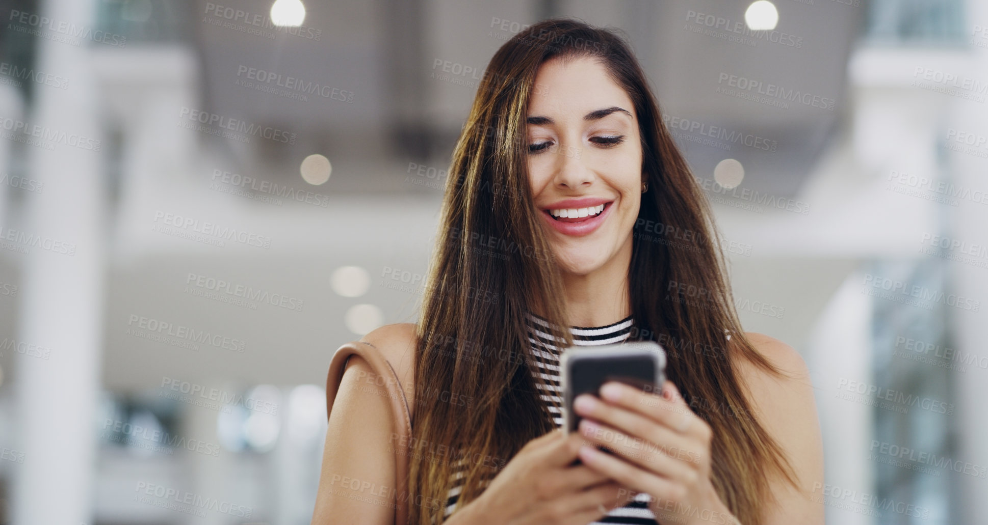 Buy stock photo Cropped shot of a young businesswoman using a smartphone while walking through a modern office