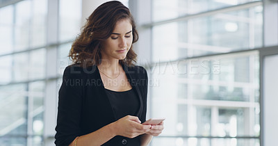 Buy stock photo Cropped shot of a confident young businesswoman using her cellphone while walking through a modern office