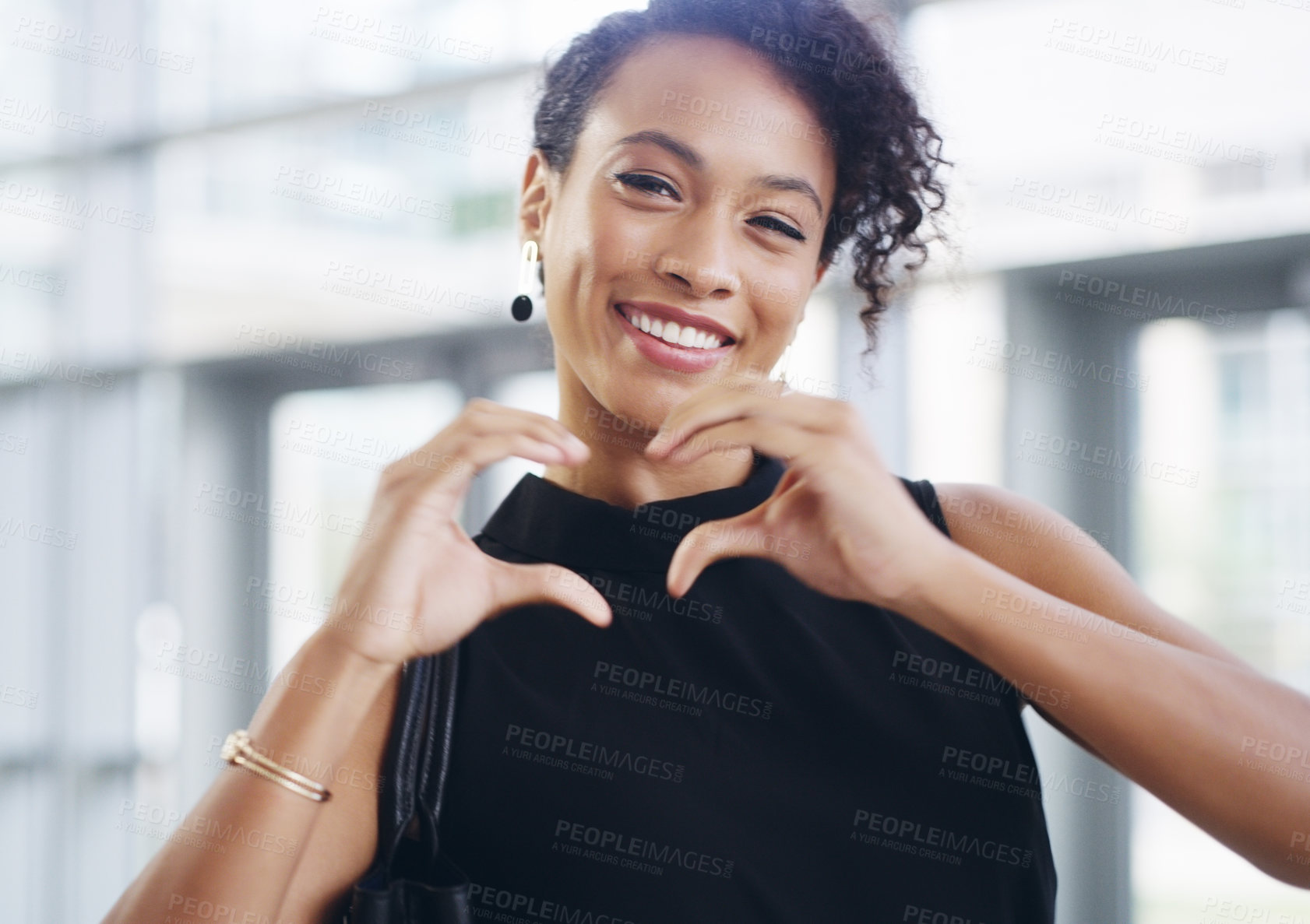 Buy stock photo Cropped shot of a young businesswoman showing a heart sign while walking through a modern office