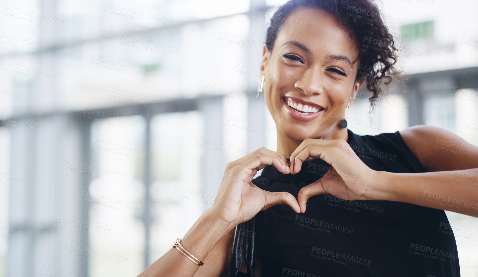 Buy stock photo Cropped shot of a young businesswoman showing a heart sign while walking through a modern office