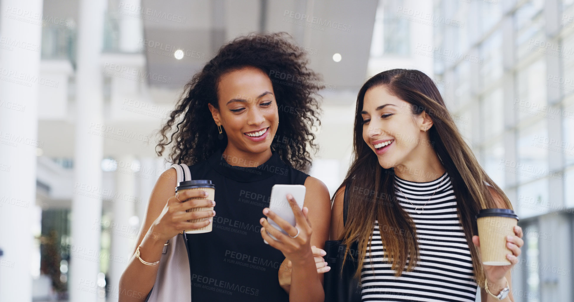 Buy stock photo Cropped shot of two young businesswomen chatting and using a smartphone while walking in an office on a coffee break