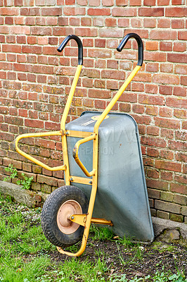 Buy stock photo Wheelbarrow against the side of a red brick wall or house. Doing gardening or cleanup work in a backyard garden on a sunny day. Professional landscapers use this equipment to move soil or dirt