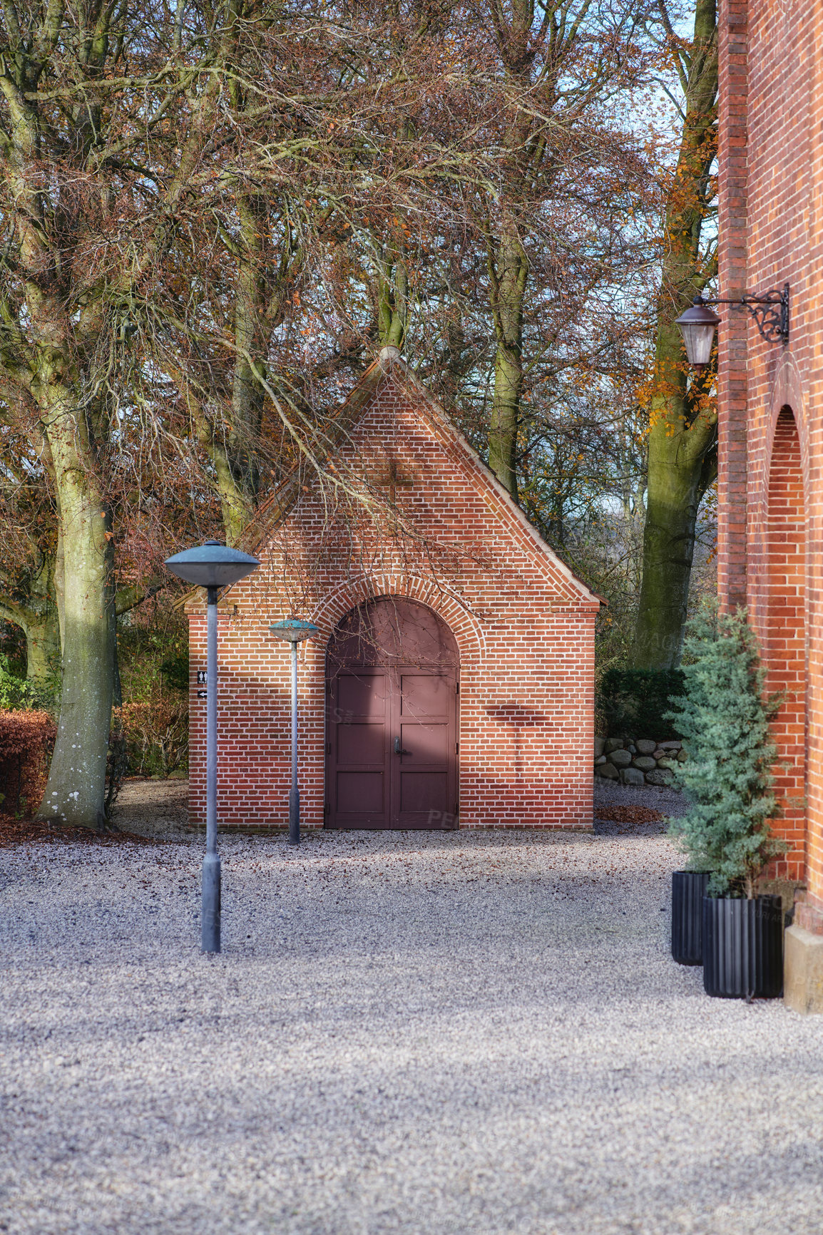 Buy stock photo Danish national church with uncultivated hardwood forest trees and plants around it and in the backyard. Red facebrick building with traditional architecture with stone courtyard and lights outside