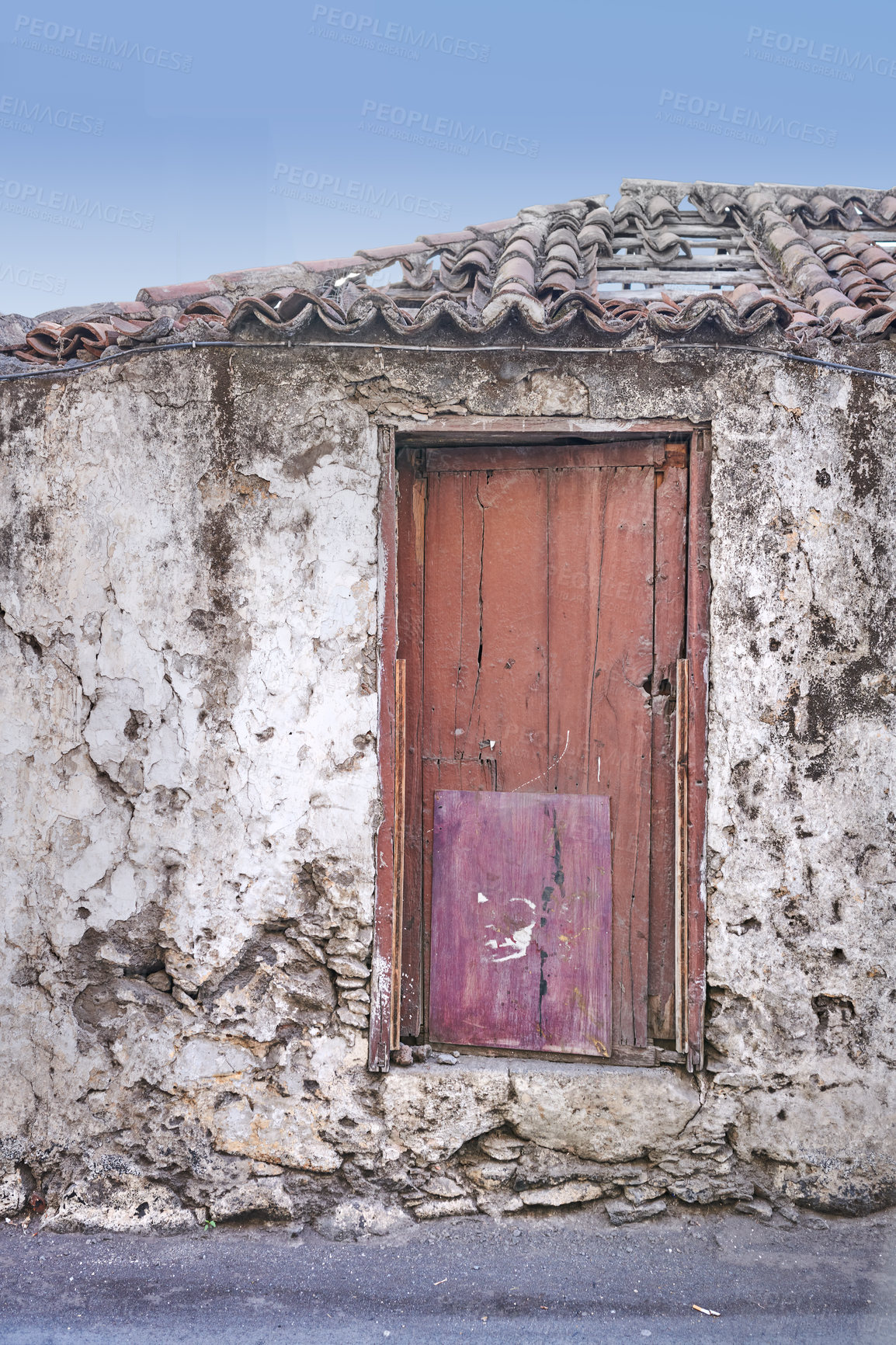 Buy stock photo Old abandoned house or home with a weathered stone wall and red wooden door. Vintage and aged residential building built in a traditional architectural style or design with a blue sky background