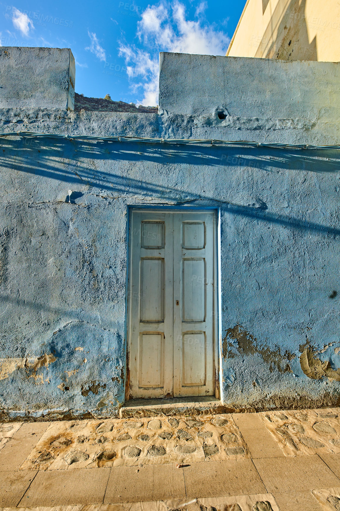 Buy stock photo Old abandoned house or home with a weathered blue wall and wooden door. Vintage and aged residential building built in a traditional architectural style or design with a blue sky background
