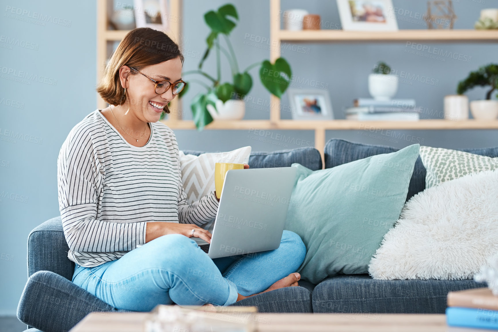 Buy stock photo Full length of a happy young woman using her laptop while relaxing on the sofa at home